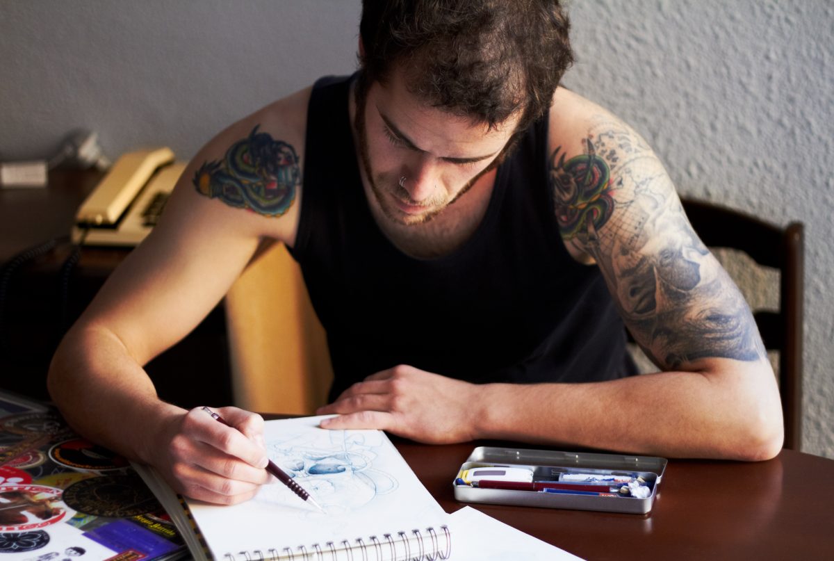 A male tattoo artist with tattoos on his arms working on his latest design concept: how to choose a tattoo