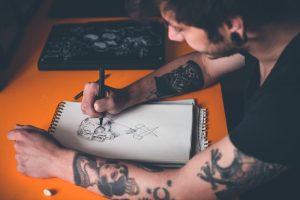 Young tattoo artist draw a new sketch on paper concept how to choose a tattoo
